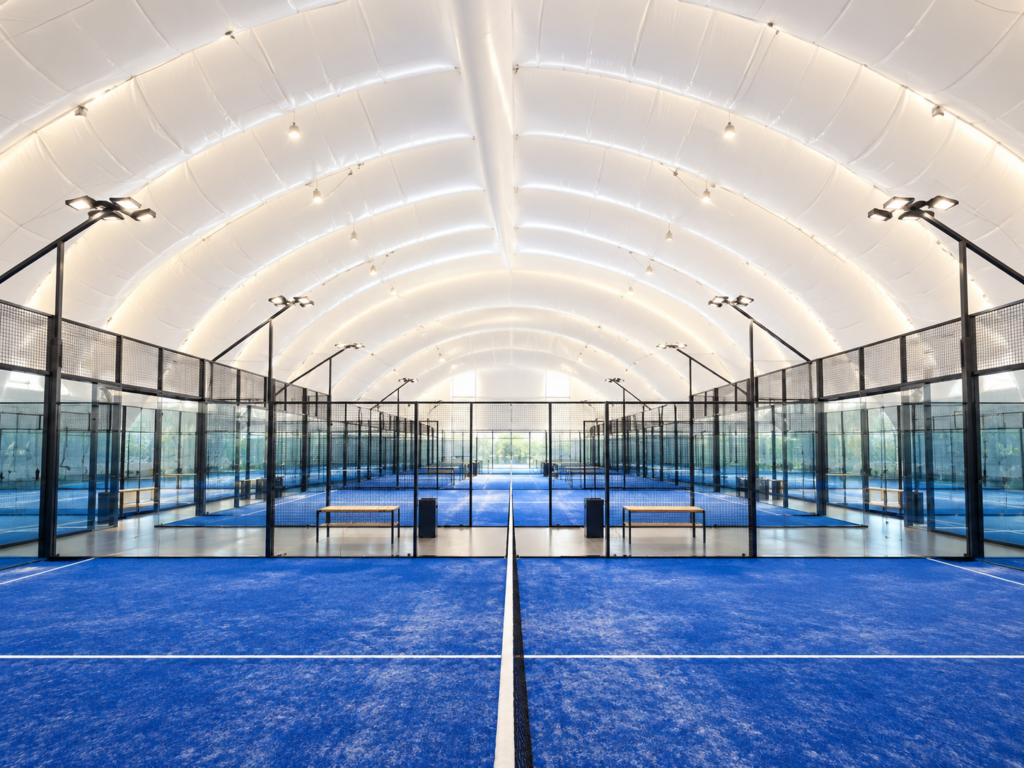 Padelhalle als Traglufthalle mit mehreren blauen Padel Courts und Flutlicht