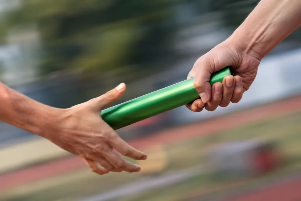 Staffelübergabe auf der Laufbahn: Eine Hand reicht den grünen Staffelstab weiter – Symbol für lückenlosen Versicherungsschutz im Sport